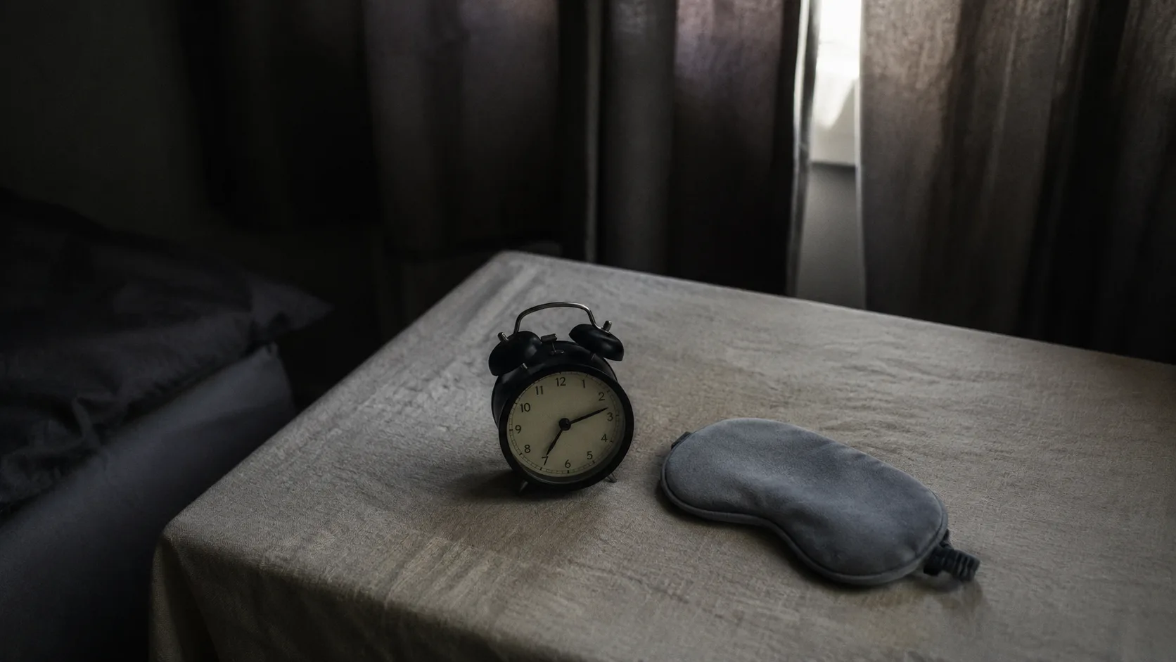 Koyu perdelerle karartılmış serin yatak odasında saat gösteren analog çalar saat ve uyku maskesi