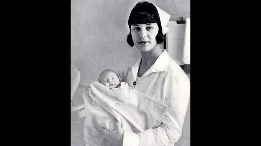 Doğum yılı 1929 olan bir bebeği kucağına alıp poz veren bir hemşire